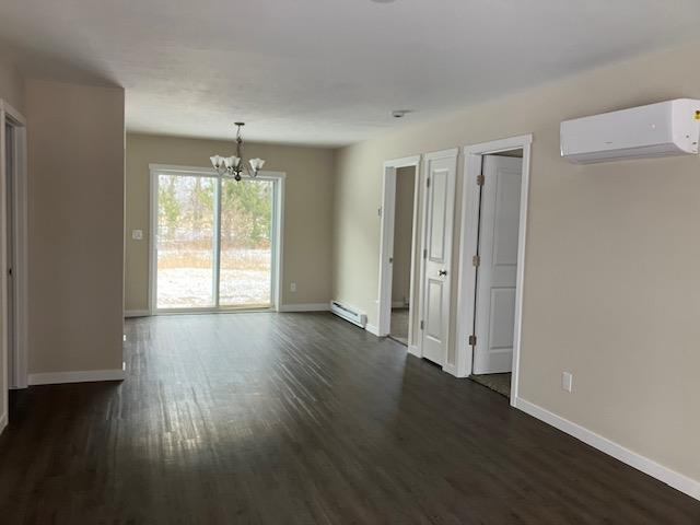 2711 Sawyer Rd, Traverse City, MI 49685 - spare room with a wall mounted AC, dark wood-type flooring, a baseboard radiator, and an inviting chandelier