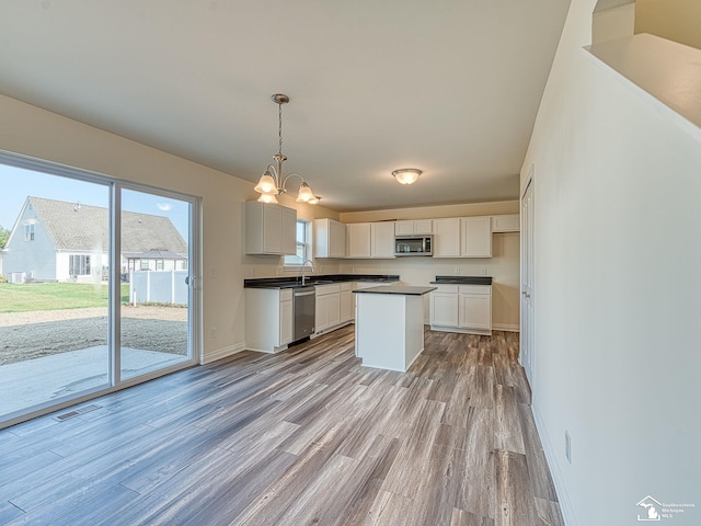 kitchen with white cabinets, decorative light fixtures, appliances with stainless steel finishes, and light hardwood / wood-style flooring