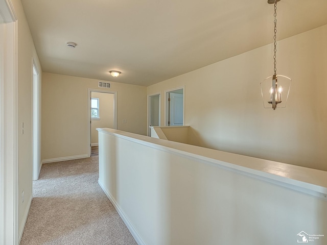 hallway featuring light colored carpet and an inviting chandelier