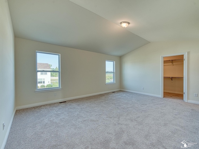 unfurnished bedroom featuring vaulted ceiling, a walk in closet, light colored carpet, and multiple windows