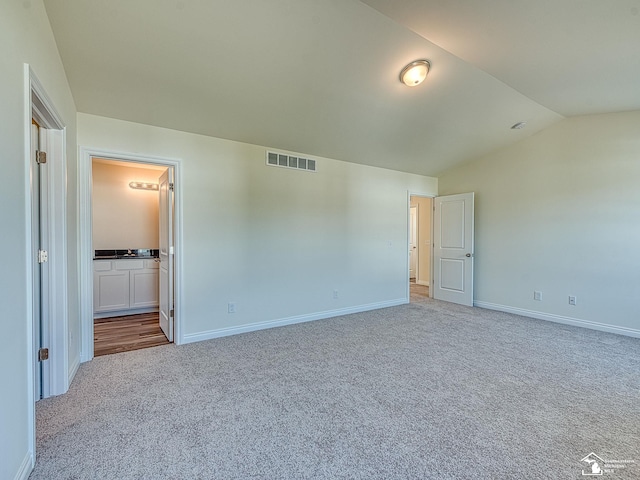 unfurnished bedroom with vaulted ceiling, light colored carpet, and ensuite bath