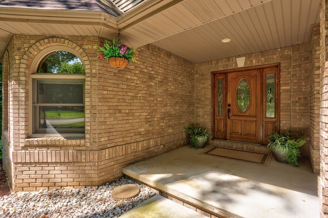 doorway to property with brick siding and roof with shingles