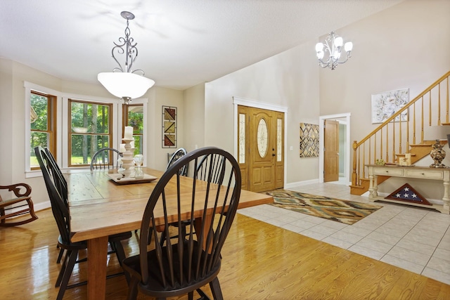 dining room with light wood-style flooring, a high ceiling, stairway, and baseboards