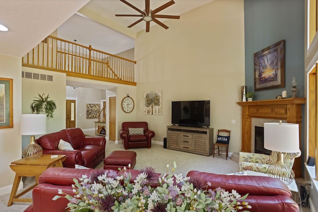 carpeted living room featuring visible vents, a fireplace with raised hearth, a towering ceiling, ceiling fan, and baseboards