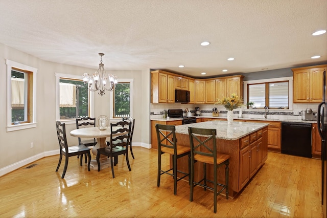 kitchen featuring a center island, visible vents, black appliances, light wood-type flooring, and a kitchen breakfast bar