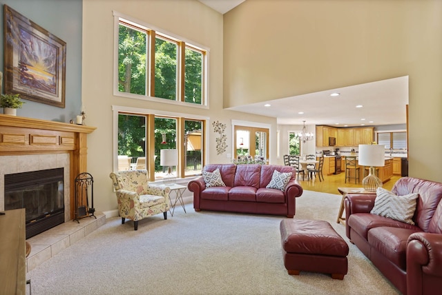 living area featuring a tile fireplace, recessed lighting, light carpet, a notable chandelier, and a high ceiling