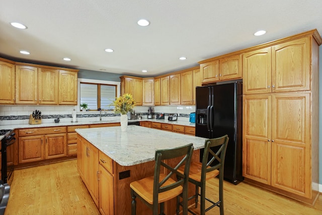 kitchen with light wood finished floors, a center island, light stone counters, and black fridge with ice dispenser