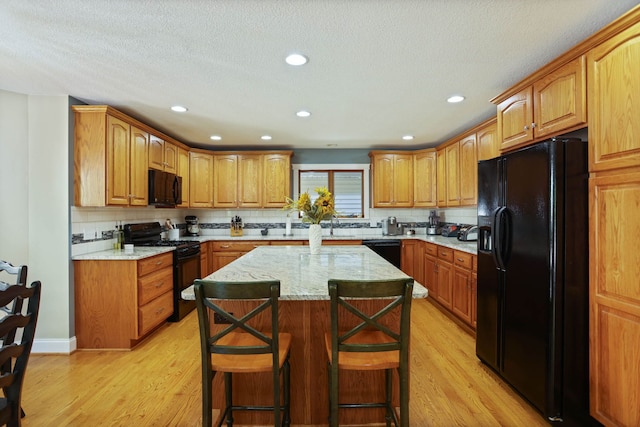 kitchen with light stone counters, a center island, brown cabinets, light wood-style floors, and black appliances