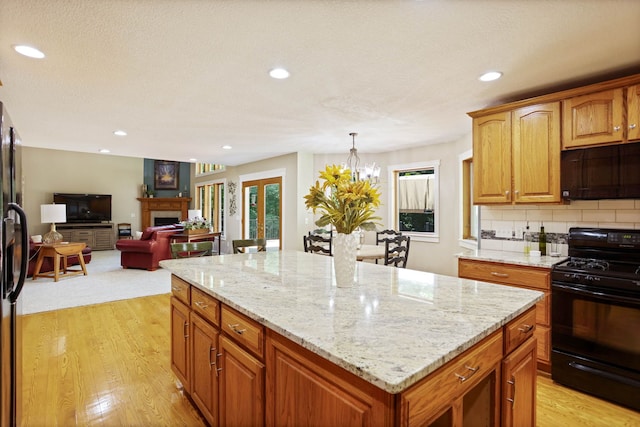 kitchen featuring black appliances, light wood finished floors, a fireplace, and a center island