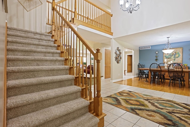 stairs with visible vents, a towering ceiling, an inviting chandelier, tile patterned flooring, and baseboards