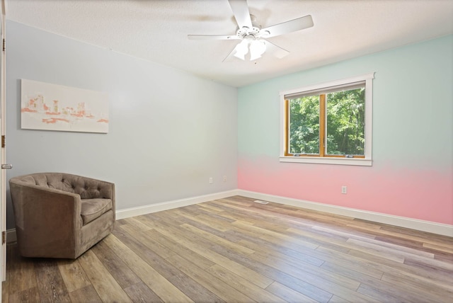 living area with wood finished floors, a ceiling fan, and baseboards