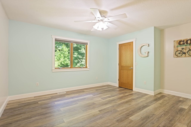 empty room with ceiling fan, a textured ceiling, baseboards, and wood finished floors