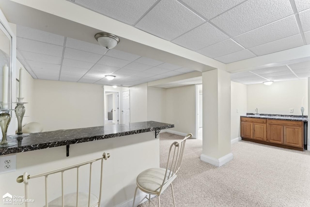 interior space with light carpet, sink, a paneled ceiling, and dark stone counters