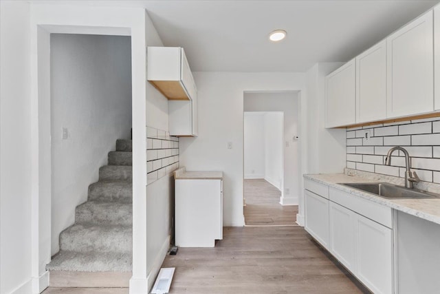 kitchen with white cabinets, sink, light stone countertops, tasteful backsplash, and light hardwood / wood-style floors