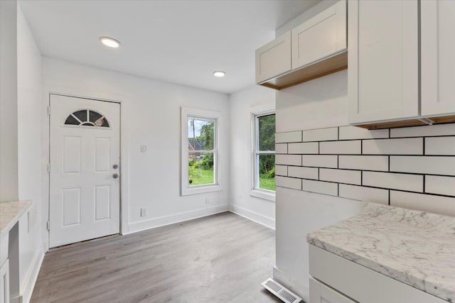 kitchen with tasteful backsplash, light stone countertops, white cabinets, and light hardwood / wood-style floors