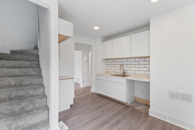 kitchen with white cabinets, light wood-type flooring, tasteful backsplash, and sink