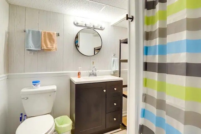 bathroom featuring a shower with curtain, a textured ceiling, toilet, wooden walls, and vanity