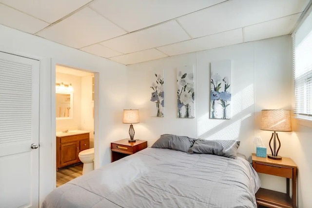 bedroom featuring connected bathroom, a paneled ceiling, and light hardwood / wood-style floors