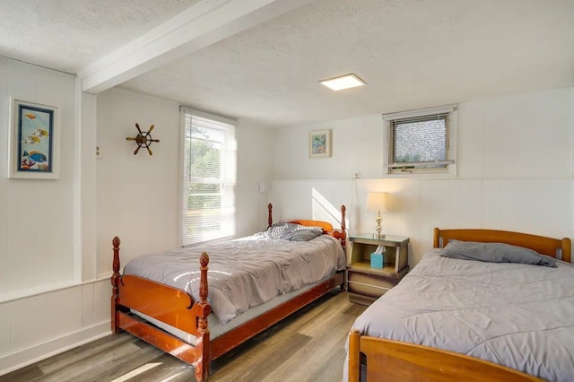 bedroom with beamed ceiling, a textured ceiling, and light wood-type flooring