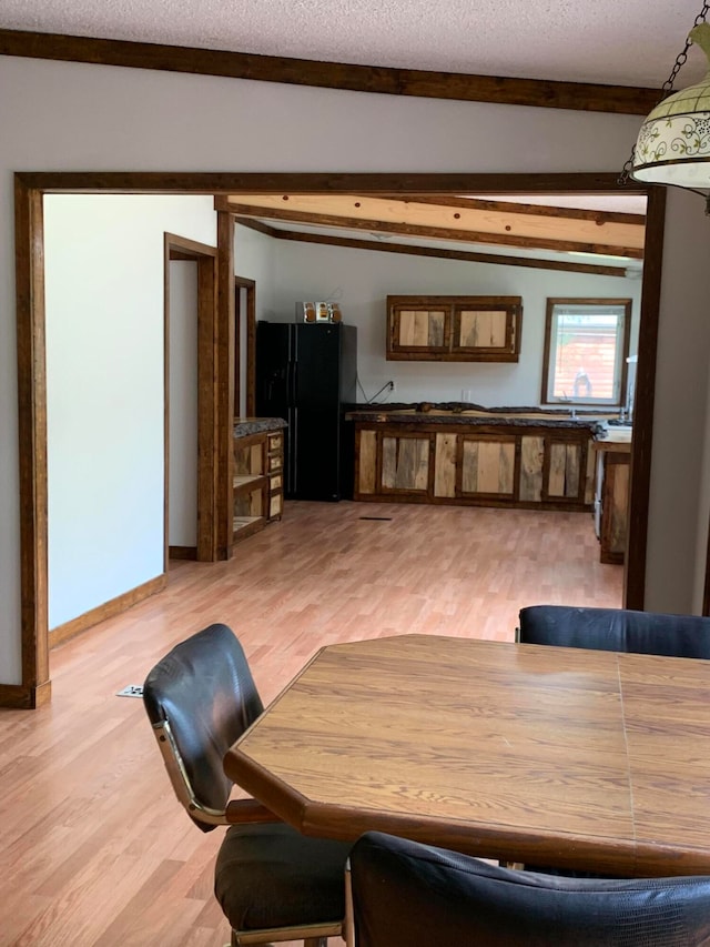 dining space featuring a textured ceiling, lofted ceiling with beams, and light hardwood / wood-style floors