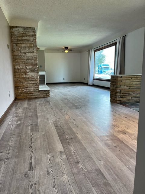 unfurnished living room featuring a stone fireplace, ceiling fan, hardwood / wood-style floors, and a textured ceiling