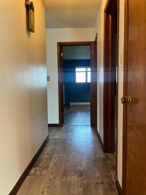 corridor featuring a textured ceiling, dark hardwood / wood-style flooring, and a baseboard heating unit