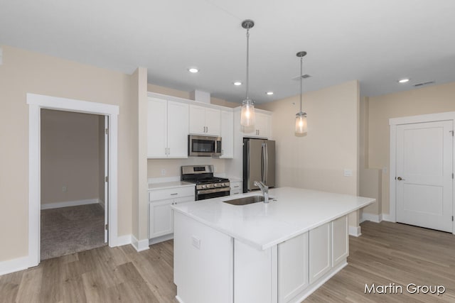 kitchen with a center island with sink, sink, hanging light fixtures, appliances with stainless steel finishes, and white cabinetry