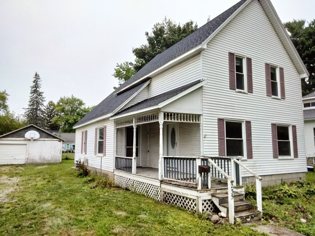 235 N Howard Ave, Croswell, MI 48422 - view of front of house with a porch, a front lawn, a shingled roof, an outdoor structure, and a detached garage