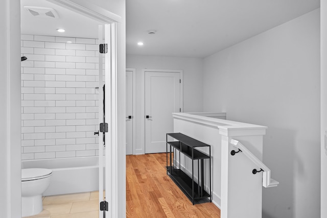 bathroom with hardwood / wood-style flooring, toilet, and tiled shower / bath