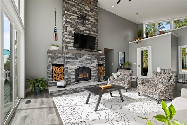 living room with a stone fireplace, ceiling fan, light hardwood / wood-style floors, and a high ceiling