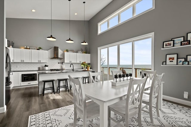 dining room featuring a water view, high vaulted ceiling, dark wood-type flooring, and sink