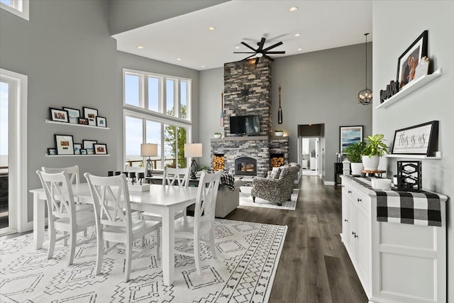 dining room featuring a fireplace, a towering ceiling, ceiling fan, and dark wood-type flooring