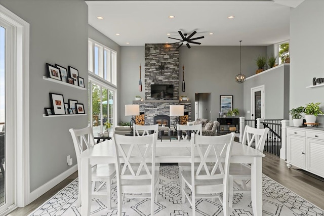 dining room with ceiling fan, a stone fireplace, light wood-type flooring, and a high ceiling