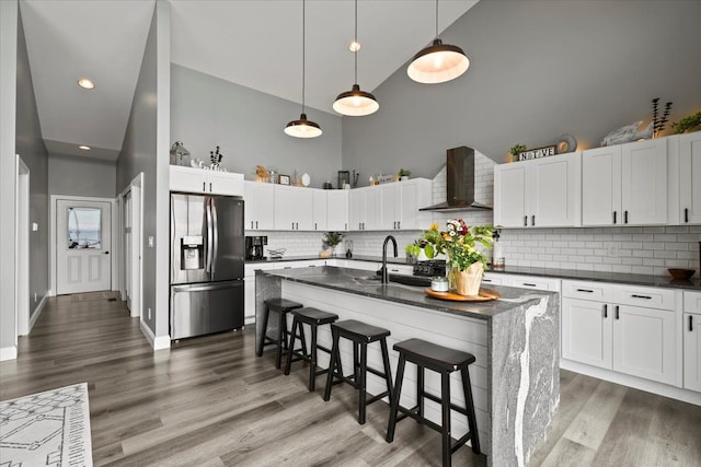 kitchen featuring wall chimney range hood, high vaulted ceiling, and stainless steel refrigerator with ice dispenser