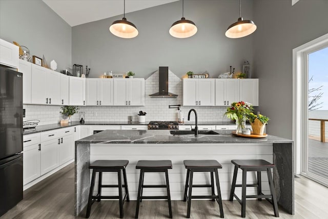 kitchen featuring dark hardwood / wood-style flooring, black fridge, sink, wall chimney range hood, and pendant lighting