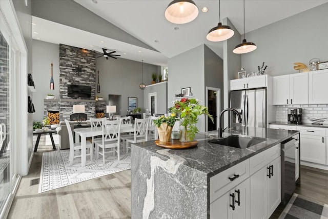 kitchen featuring sink, stainless steel refrigerator with ice dispenser, dark stone countertops, a fireplace, and an island with sink