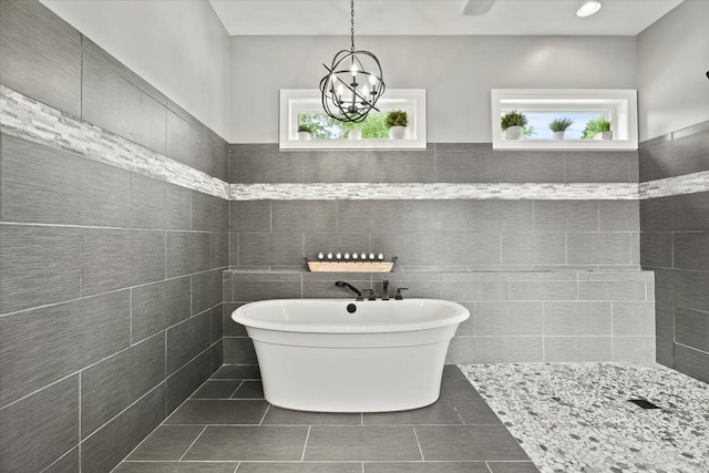 bathroom featuring a bathing tub, tile walls, a wealth of natural light, and an inviting chandelier