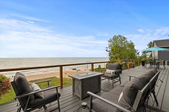 wooden terrace featuring a fire pit, a water view, and a beach view