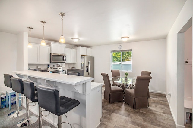 kitchen with kitchen peninsula, appliances with stainless steel finishes, wood-type flooring, decorative light fixtures, and white cabinetry