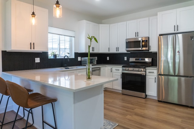 kitchen featuring white cabinets, hanging light fixtures, light hardwood / wood-style floors, kitchen peninsula, and stainless steel appliances