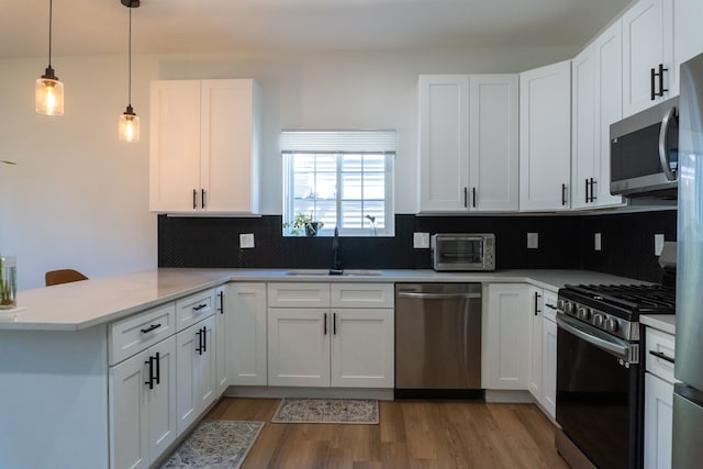 kitchen with hanging light fixtures, kitchen peninsula, appliances with stainless steel finishes, white cabinets, and hardwood / wood-style flooring