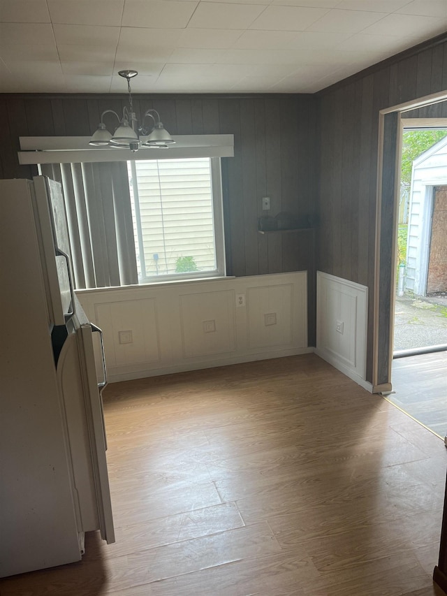 unfurnished dining area with a notable chandelier, wood walls, and light wood-type flooring