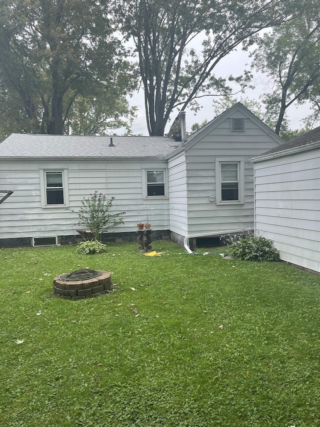 rear view of property featuring a fire pit and a lawn