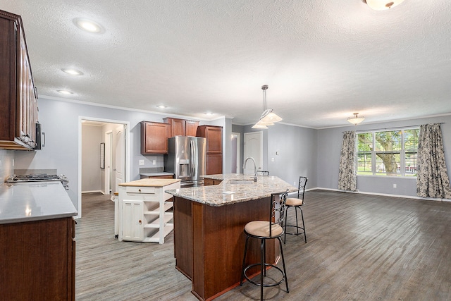 kitchen with a kitchen island with sink, sink, a textured ceiling, decorative light fixtures, and stainless steel appliances