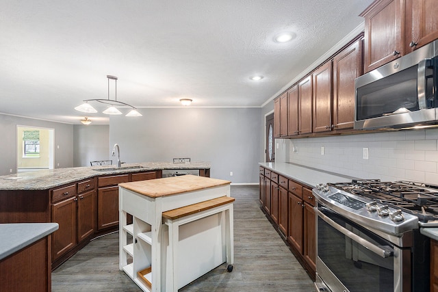 kitchen with appliances with stainless steel finishes, decorative light fixtures, dark wood-type flooring, and sink