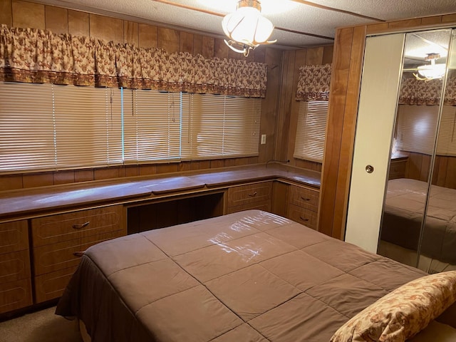 bedroom with a textured ceiling, built in desk, carpet floors, a closet, and wood walls