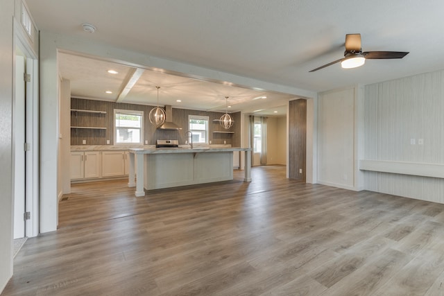 unfurnished living room featuring ceiling fan with notable chandelier, beam ceiling, sink, and light hardwood / wood-style flooring