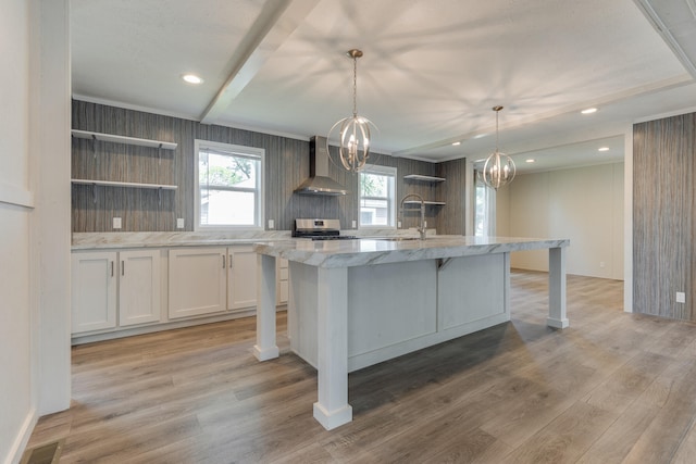 kitchen featuring pendant lighting, white cabinets, a center island with sink, wall chimney range hood, and stainless steel range oven