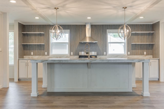 kitchen featuring dark wood-type flooring, wall chimney range hood, decorative light fixtures, an inviting chandelier, and white cabinetry