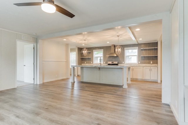 kitchen with light wood-type flooring, a kitchen island, hanging light fixtures, and wall chimney exhaust hood